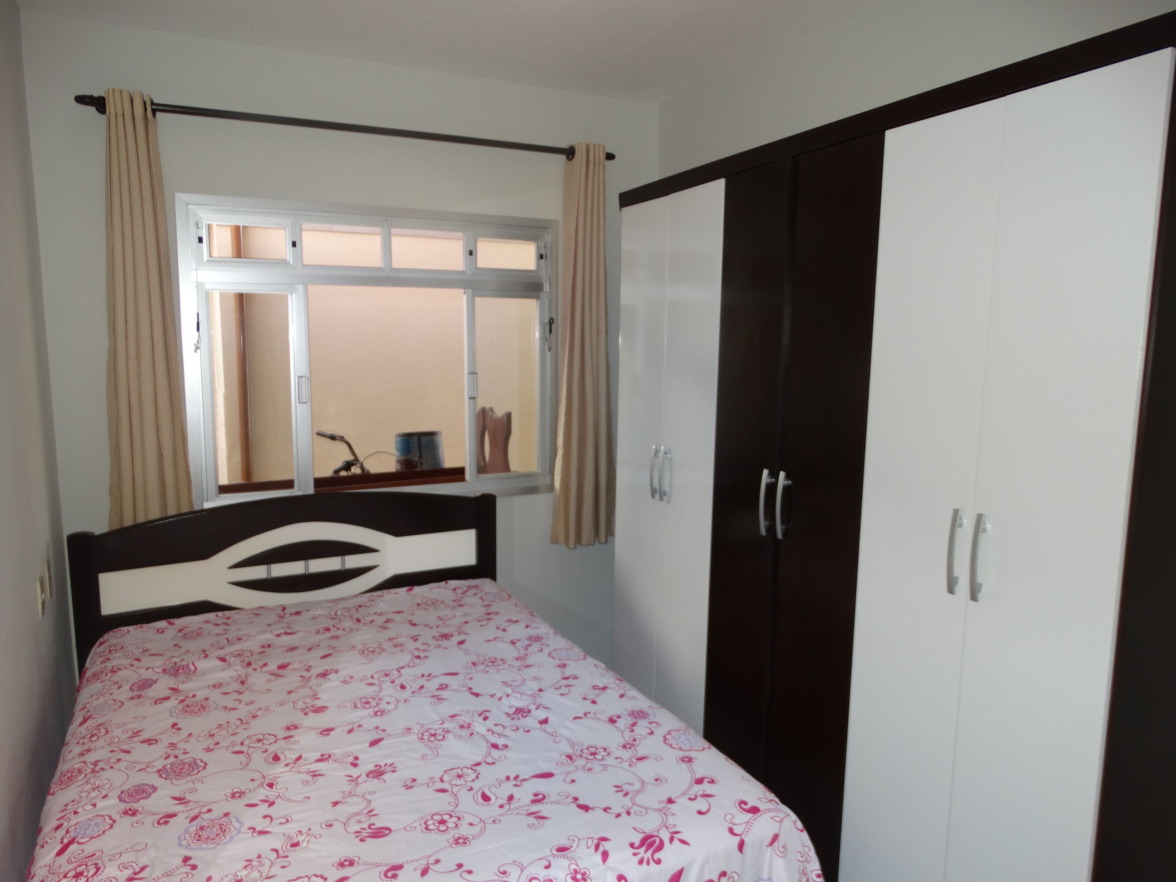 A bedroom with a bed, a wardrobe, a window with curtains, and a mirror.