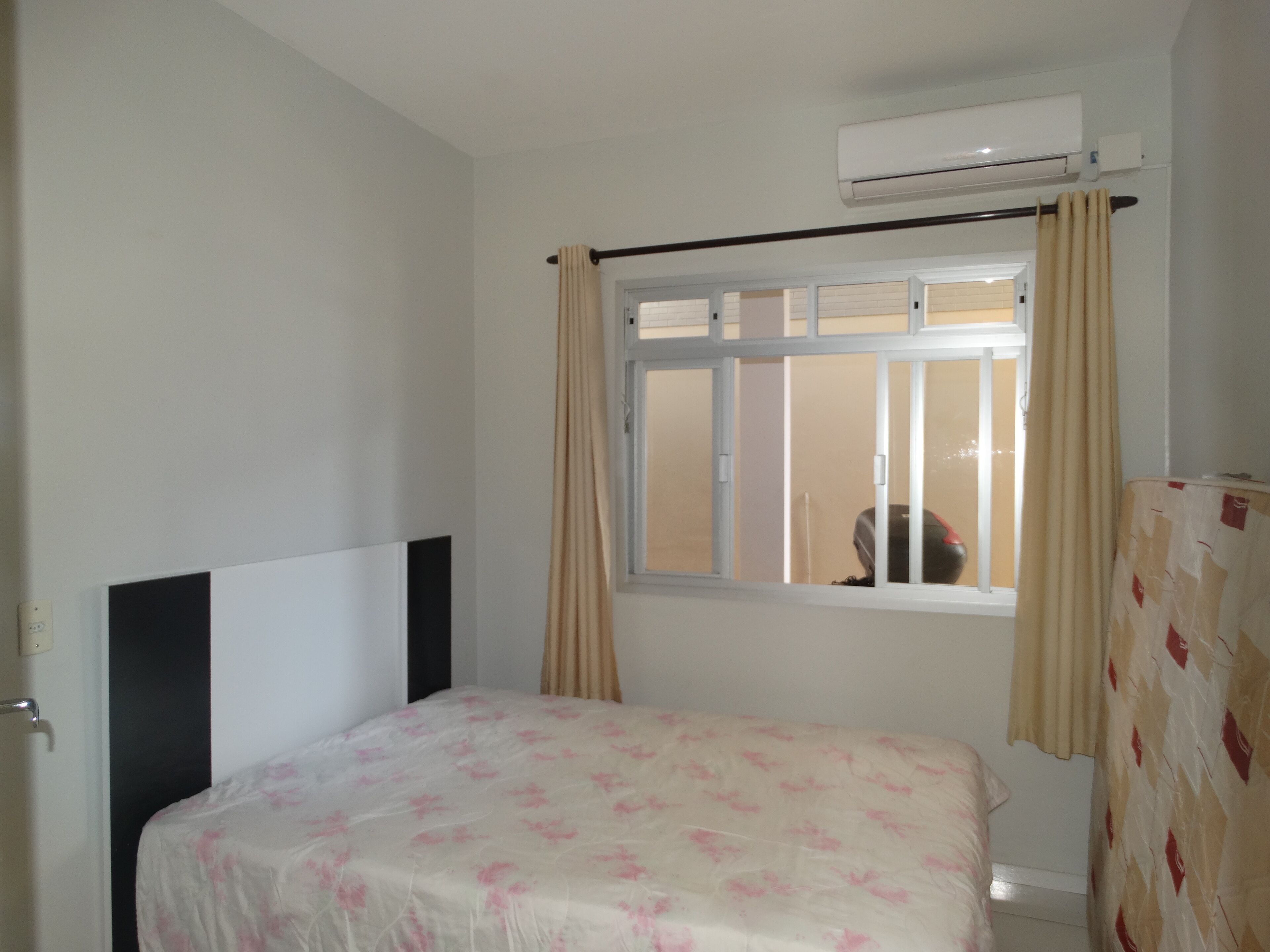 A bedroom with a bed, a window with curtains, an air conditioning unit, and a door.