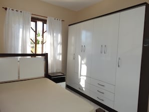 Quarto com cama, guarda-roupa e janela com cortinas.