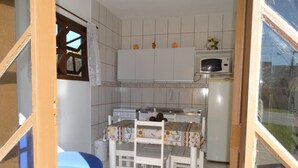Een kleine keuken met witte kasten, een magnetron en een eettafel met stoelen.