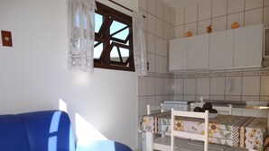 Een kamer met een blauwe bank, een eettafel met stoelen, een keuken met een fornuis en een raam met kantgordijnen.