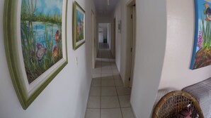 A hallway with tiled flooring, framed paintings on the walls, and a wicker basket on the right. - House 4D, 100m From the Sea - 229 (Florianópolis)