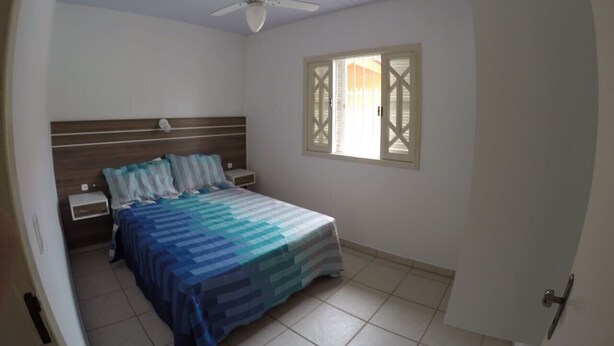 A bedroom with a bed, nightstands, a ceiling fan, and a window with shutters. - House 4D, 100m From the Sea - 229 (Florianópolis)