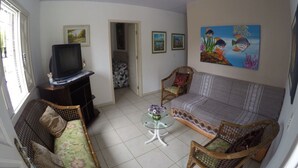 A living room with a sofa, two wicker chairs, a glass coffee table, a television on a stand, and framed pictures on the walls. - House 4D, 100m From the Sea - 229 (Florianópolis)