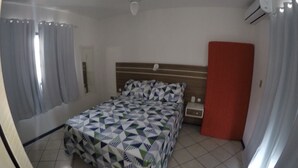 Ein Schlafzimmer mit einem Bett, einem Nachttisch, einer roten Tür und einer Klimaanlage.