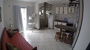 Ein kompakter Wohnraum mit Küchenzeile, einem Essbereich mit Hockern, einer Wendeltreppe und einem Bett mit Kissen.