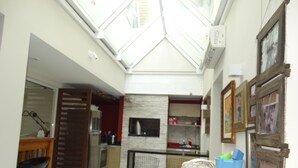 A compact kitchen with a built-in stove, a dining area with a wooden table and chairs, and a skylight above. - House on the Sand - 219 (Florianópolis)