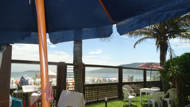 An outdoor seating area with tables and chairs, a view of the beach, and a palm tree. - House on the Sand - 219 (Florianópolis)