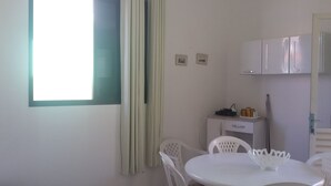 A small, clean room with a single white table and chairs, a small cabinet, and a window with curtains. - Apartment 1D, 50m From the Sea - 65 (Florianópolis)