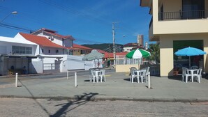 A street view with a building that has a sign reading "Petria". There are outdoor tables and chairs, and a green and white striped umbrella. - Apartment 1D, 50m From the Sea - 65 (Florianópolis)