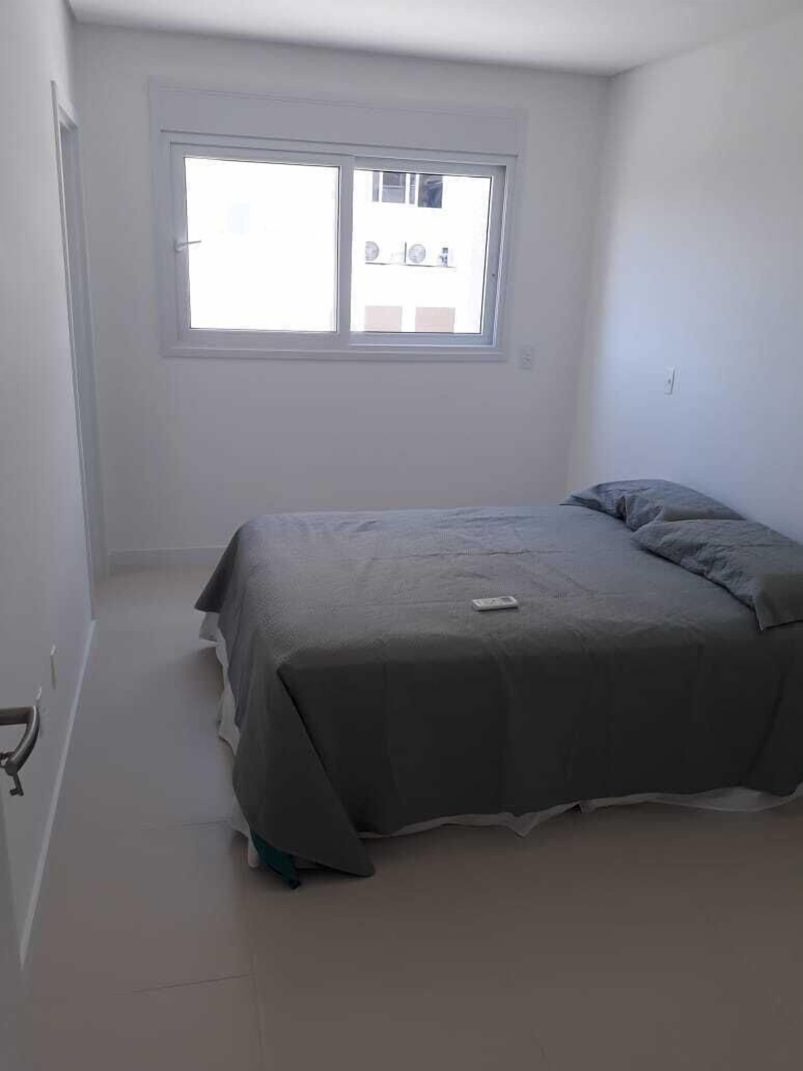 A small, sparsely furnished room with a single bed, a window, and a door.