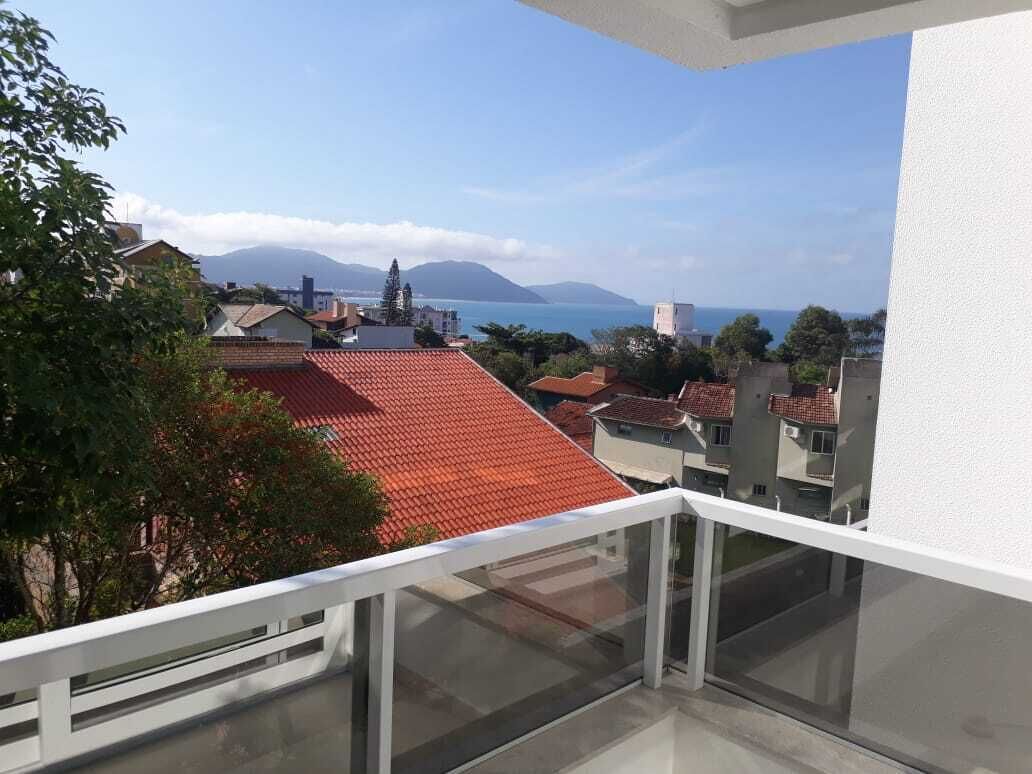 A balcony with a view of a coastal town, red-roofed buildings, and distant mountains.