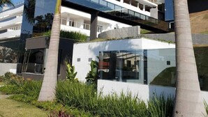 A modern building with a glass facade, a pedestrian bridge, and palm trees. - Apartment with Infinity Pool & Panoramic Views - 228 (Florianópolis)