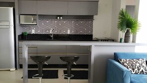 A modern kitchen with a refrigerator, a microwave, and a patterned backsplash. There is a bar area with stools and a blue sofa with a patterned pillow. - Apartment with Infinity Pool & Panoramic Views - 228 (Florianópolis)
