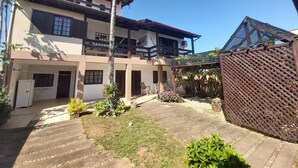 A two-story house with a balcony, a garden with stepping stones, and a wooden fence. - Large Pool House in Campeche - 109 (Florianópolis)