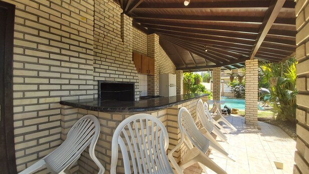 An outdoor patio with a brick wall, a grill, and white plastic chairs. - Large Pool House in Campeche - 109 (Florianópolis)