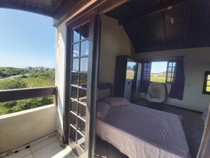 A bedroom with a bed, a wardrobe, and a window with a view of greenery and buildings.