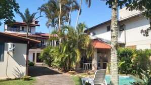 A residential area with a paved pathway leading to a pool area, surrounded by palm trees and a white building with a red roof. - Large Pool House in Campeche - 109 (Florianópolis)