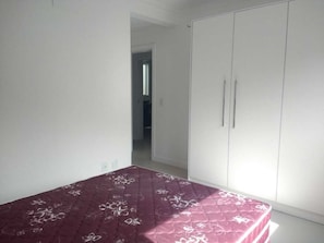 Quarto com cama, guarda-roupa branco e porta para outro cômodo.