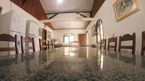 A dining area with a large granite table, wooden chairs, a white refrigerator, and a painting on the wall.