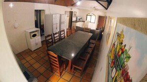 A compact kitchen with a dining area, featuring a tiled floor, a refrigerator, a microwave, and a painting of fruits on the wall.