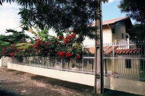 Una casa con fachada blanca, tejado de tejas rojas y valla blanca adornada con flores rojas.