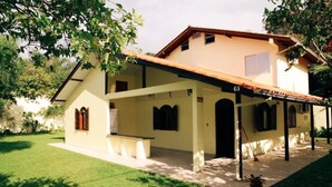 A two-story house with a covered patio, a small garden, and a number '65' on the facade.