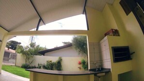 A covered outdoor kitchen area with a counter, sink, and cabinets.