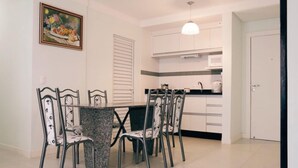 A dining area with a table and chairs, a kitchen in the background, and a door to the right. - 2 Bedroom Apartment - 201 (Florianópolis)