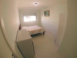 Quarto pequeno com uma cama de solteiro, janela, escrivaninha e porta.