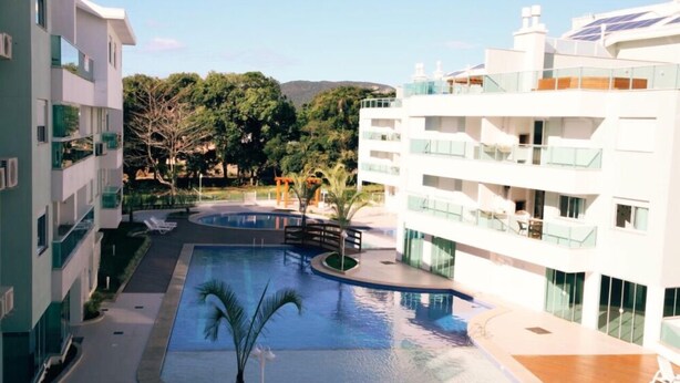 A modern hotel with a pool area, multiple balconies, and a view of the surrounding greenery. - 2 Bedroom Apartment - 202 (Florianópolis)