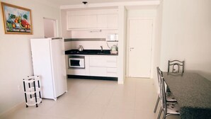 A compact kitchen with white cabinets, a refrigerator, and a microwave. There is a small dining area with a table and chairs. - 2 Bedroom Apartment - 202 (Florianópolis)
