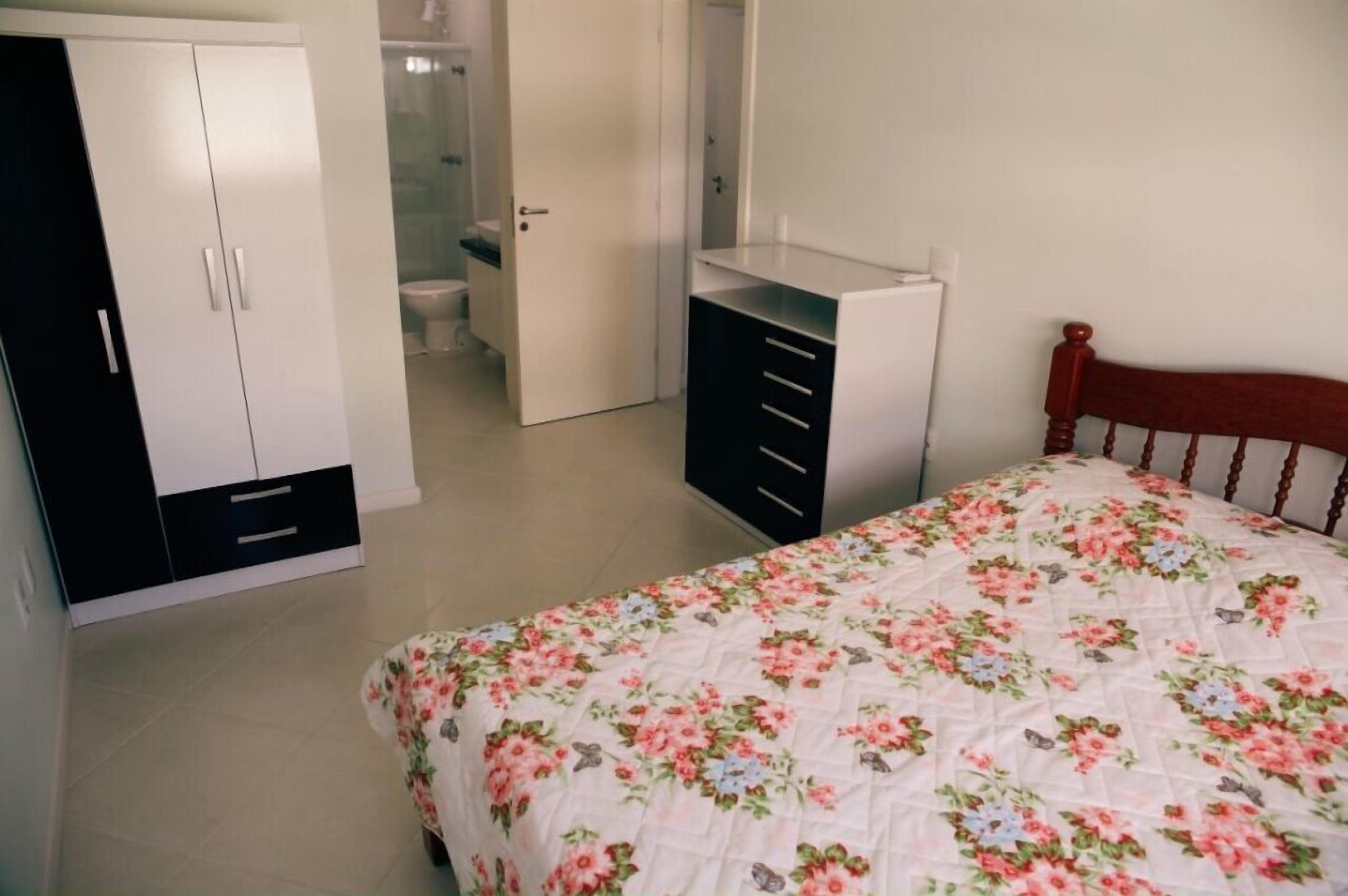 A bedroom with a bed, a wardrobe, a desk, and a bathroom in the background.