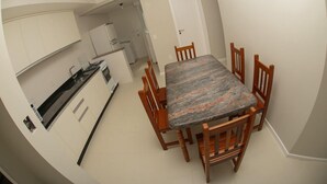 Eine kompakte Küche mit weißen Schränken, einem Esstisch mit sechs Holzsesseln und einem kleinen Kühlschrank.