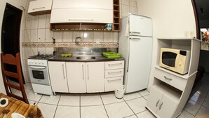Een kleine keuken met witte kastjes, een fornuis, een spoelbak en een magnetron.