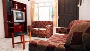 Ein Wohnzimmer mit Fernseher auf einer Holzeinrichtung, einem gemusterten Sofa und einem Glastisch.