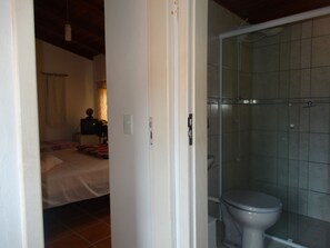 Un baño con ducha, inodoro y una cama en la habitación contigua.