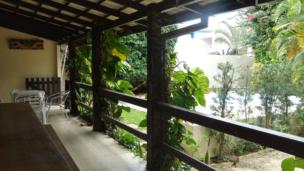Un espacio al aire libre cubierto con una mesa y sillas de madera, rodeado de vegetación exuberante y vistas a una zona residencial.