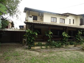 Un edificio de dos pisos con un balcón, rodeado de follaje.