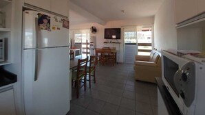 Cocina compacta con refrigerador, microondas y horno. Cuenta con un comedor con sillas y una mesa, y un televisor montado en la pared.