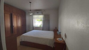 Un dormitorio con cama, escritorio con lámpara, armario y ventana con cortinas.