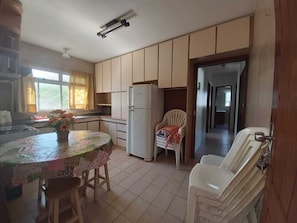 A kitchen with a dining table, chairs, a refrigerator, and a chair with a blanket. - House 3D, 250m From the Sea - 247 (Florianópolis)