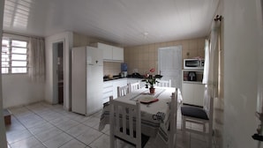 A compact kitchen with white cabinets, a refrigerator, a microwave, and a dining table with chairs. - Casa Pé na Areia, 2D, C Ar - Ingleses 41 (Florianópolis)