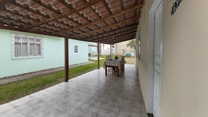 A covered patio area with a tiled floor, a table with chairs, and a small garden visible through the open end. - Casa Pé na Areia, 2D, C Ar - Ingleses 41 (Florianópolis)