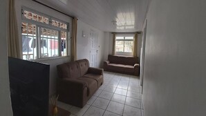 A room with a brown sofa, a TV, and a tiled floor. - Casa Pé na Areia, 2D, C Ar - Ingleses 41 (Florianópolis)