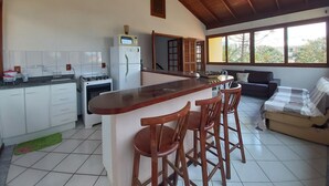 Une cuisine spacieuse dotée d’un îlot central, un coin repas avec un canapé et des fauteuils, et de grandes fenêtres offrant une vue sur l’extérieur.