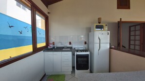 Une cuisine compacte avec des meubles blancs, un four à micro-ondes, un four encastré et une fenêtre donnant sur la mer.