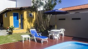 Un espace piscine avec une piscine bleue, des chaises longues blanches et une table avec des chaises.