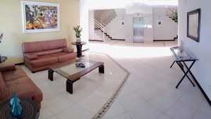 A spacious lobby with a brown leather sofa, a glass coffee table, and a small table with a plant. A staircase and elevator are visible in the background. - Ap Premium na Lagoa (Florianópolis)