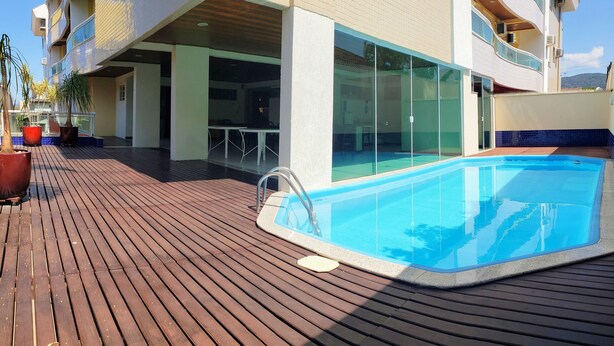 A pool area with a wooden deck, a glass-enclosed balcony, and potted plants. - Ap Premium na Lagoa (Florianópolis)